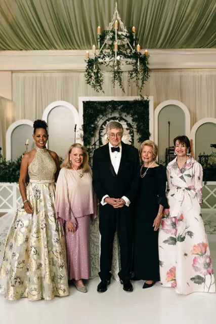 Five people in formal attire pose in front of a decorated backdrop.