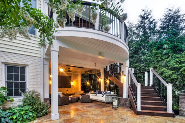 Covered patio with swing, outdoor seating, and stairs leading to a balcony.