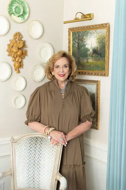 Woman in brown dress standing next to a chair with blue patterned upholstery.