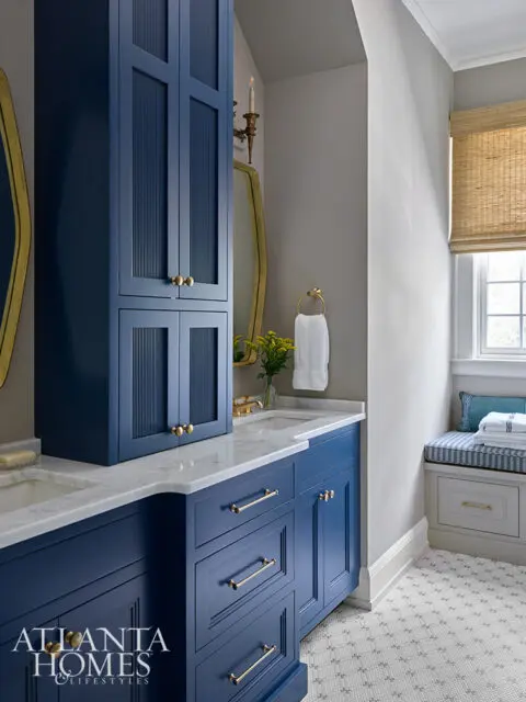 Blue bathroom vanity with marble countertop and brass hardware. Tall cabinet with fluted doors.