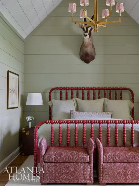 Bedroom with red spindle bed, taxidermy antelope head, and patterned benches.