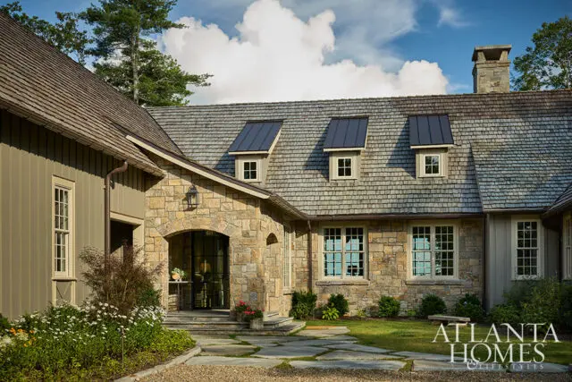Stone and wood-sided house with arched entryway, dormer windows, and stone chimney.