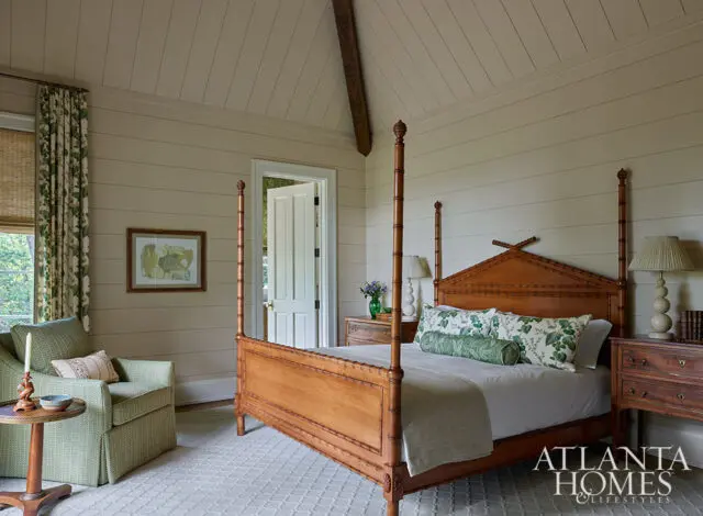 Bedroom with wood four-poster bed, green patterned pillows, and shiplap walls.