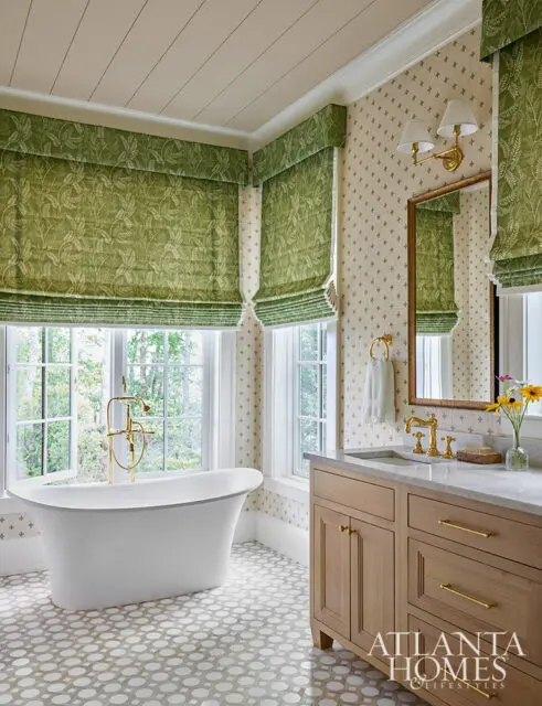 White freestanding tub, wood vanity, and green floral Roman shades in a bathroom.