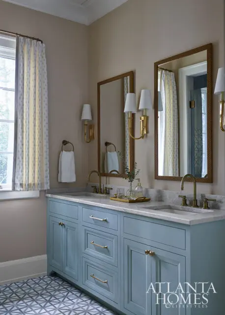 Blue vanity with marble countertop, brass fixtures, and two mirrors. Geometric floor tiles.