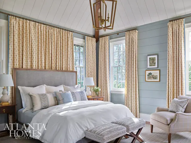 Bedroom with gray upholstered headboard, white bedding, patterned curtains, and shiplap walls.