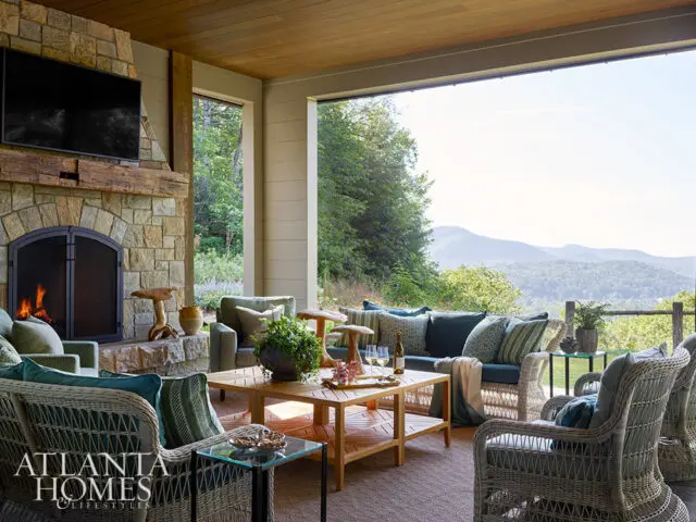 Covered porch with stone fireplace, wicker furniture, and mountain view.