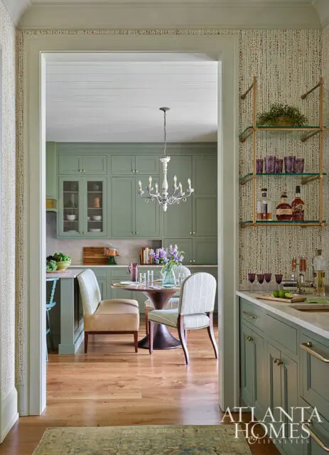 Green kitchen with round dining table, chairs, and bar cart with bottles and glassware