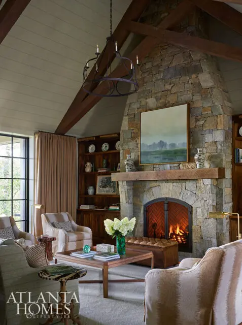 Living room with stone fireplace, wood beams, built-in bookshelves, and upholstered seating.