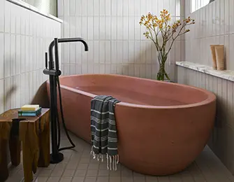 Terracotta bathtub with black faucet, next to a wooden stool and striped towel.