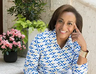 Woman with dark hair smiling, wearing a blue and white patterned shirt and gold watch.