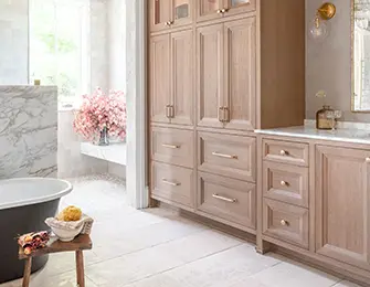 Light wood cabinetry with brass hardware in a bathroom with a black tub and marble accents.