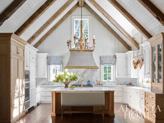 White kitchen with marble counters, wood beams, and a large island with a bench seat.