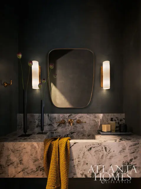 Dark powder room with marble vanity, brass fixtures, and modern sconces.