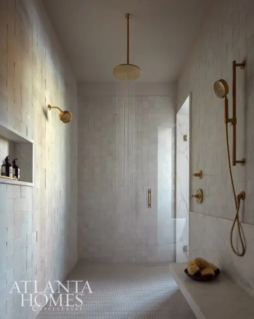 Modern bathroom with white tile walls, brass fixtures, and a glass shower enclosure.