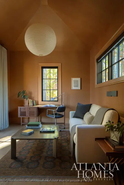 Office with tan grasscloth walls, large paper lantern, desk, and sofa.