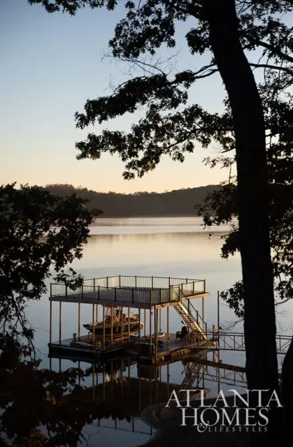 Dock with boat on a calm lake at sunrise, framed by trees.