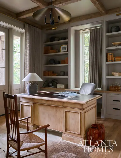 Office with wood desk, leather chair, built-in bookshelves, and pendant light.
