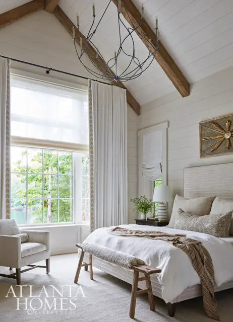 Bedroom with vaulted wood-beamed ceiling, white bedding, and large window overlooking trees and