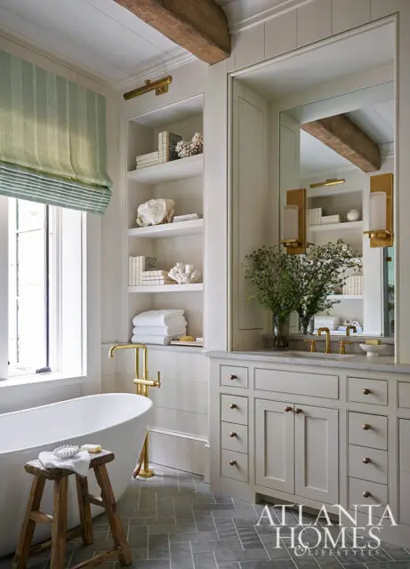 Cream bathroom with freestanding tub, wood stool, and double vanity with brass fixtures.