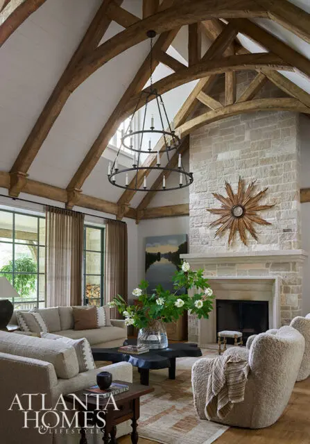 Living room with vaulted wood beam ceiling, stone fireplace, and neutral upholstered furniture.