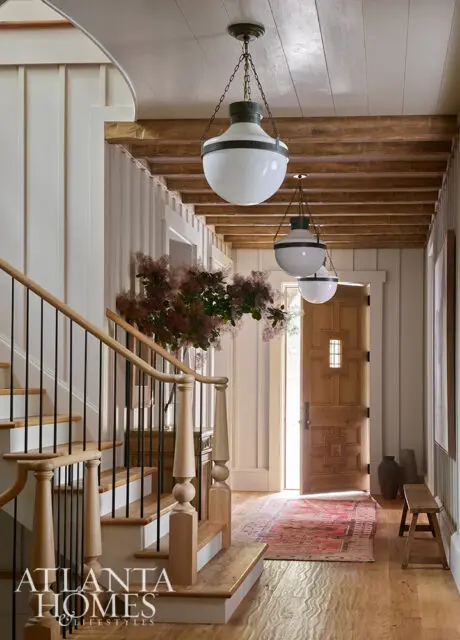 Hallway with wood staircase, paneled walls, beamed ceiling, and pendant lights.
