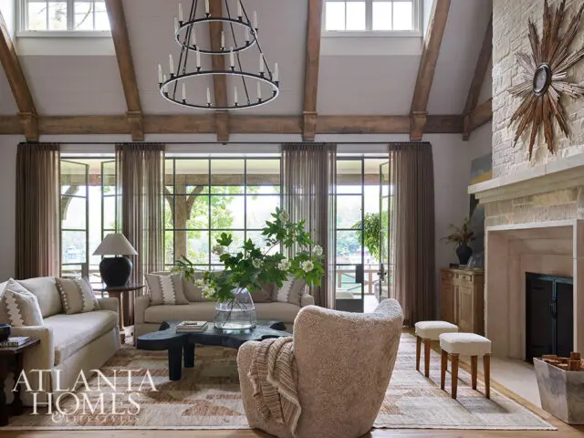 Living room with vaulted beamed ceiling, stone fireplace, and large windows overlooking water.