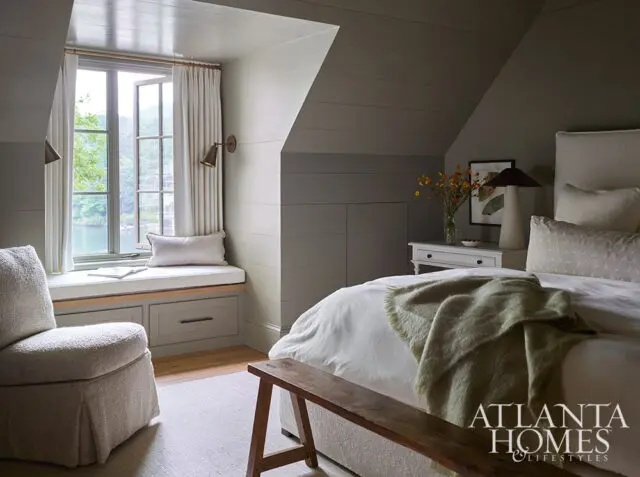 Bedroom with a window seat, upholstered chair, and bed with a green throw.