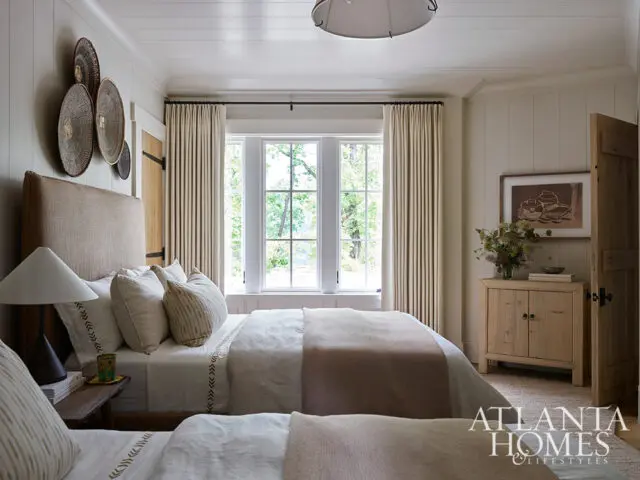 Bedroom with beige walls, linen bedding, and window view.