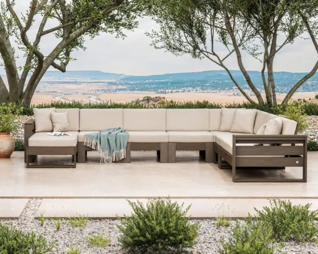 Sectional outdoor sofa with beige cushions and a teal throw blanket on a patio with a scenic view.