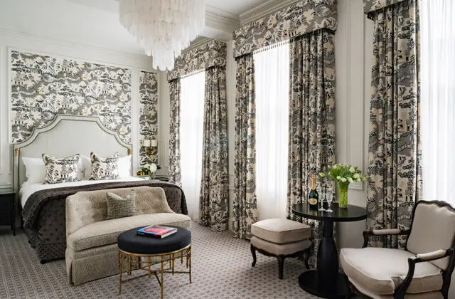 Bedroom with toile wallpaper, ornate headboard, tufted sofa, and patterned carpet.