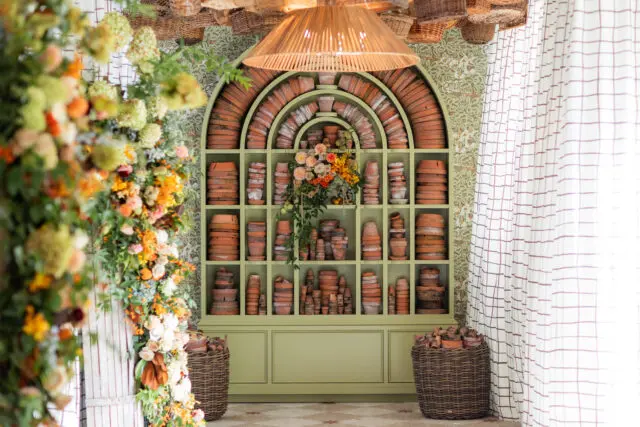 Green arched shelving unit filled with pottery and flowers.