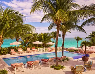 Resort pool with lounge chairs and umbrellas, palm trees, and ocean view