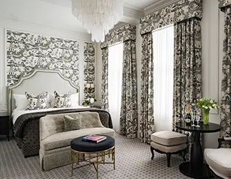 Bedroom with patterned wallpaper and curtains, tufted headboard, and crystal chandelier.
