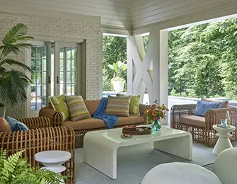 Covered porch with wicker furniture, white coffee table, and colorful striped pillows.