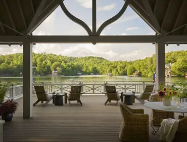 Covered porch with wicker chairs and table overlooking a lake and wooded hills