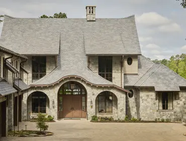 Stone house with arched entryway, multiple gables, and dormer windows.