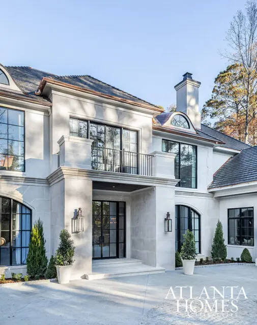 Stone facade home with black framed windows and arched doorway, manicured landscaping.