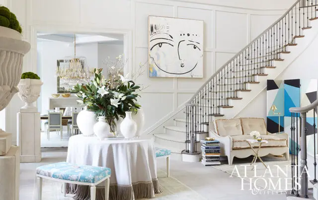 White foyer with staircase, abstract art, and a console table with floral arrangement.