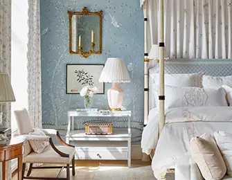 Blue bedroom with four-poster bed, floral wallpaper, and antique mirror.