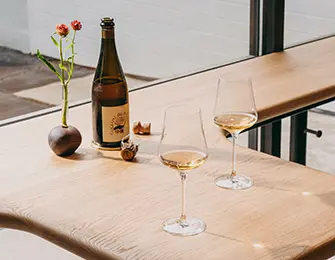 Wooden table with wine bottle, two glasses, and small vase with flowers.