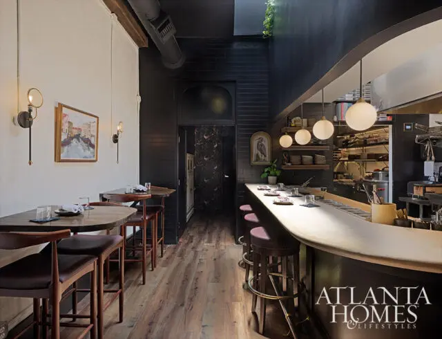 Dark kitchen and dining area with wood floors, black tile, and brass wall sconces.