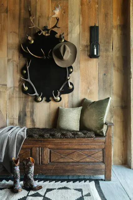 Rustic wooden wall paneling, antler mirror, and a velvet cushion.