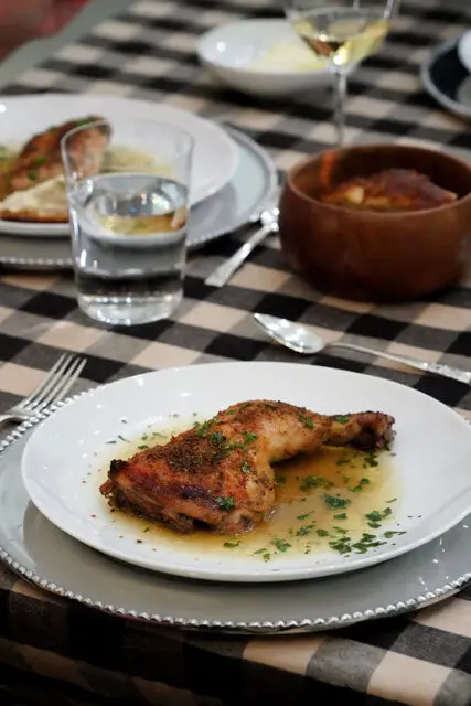 Roasted chicken on a white plate with herbs, set on a checkered tablecloth.