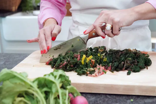 Hands chopping chard on a wooden cutting board with a Boker knife.