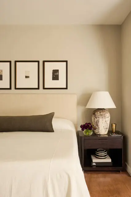 Neutral bedroom with a beige headboard, framed artwork, and a bedside table.