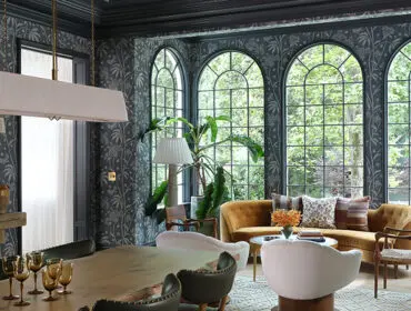 Dark wallpapered room with arched windows, mustard velvet sofa, and a wooden table.