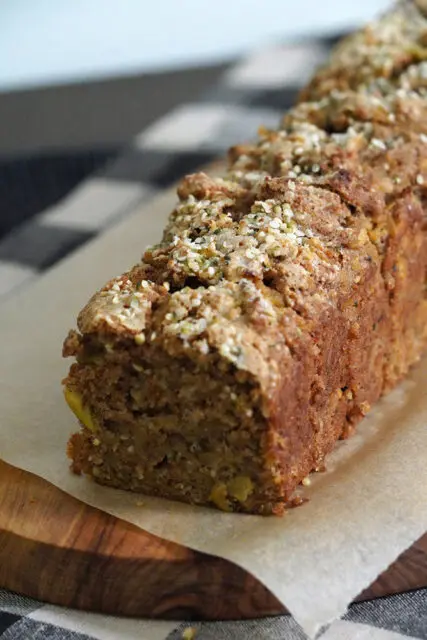 Sliced spiced bread with seeds and nuts on parchment paper and wooden board.