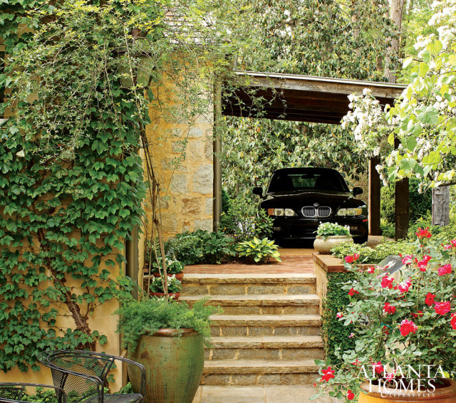 Stone steps lead to a carport with a black car parked inside, surrounded by lush greenery and red roses.