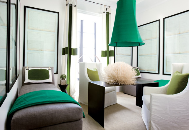 Gray chaise lounge with emerald green throw and pillow, white armchair, and large green pendant light in a room with framed documents on the wall.